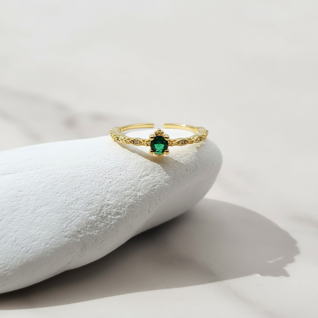 Gold ring with a green gemstone on a white stone surface