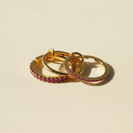 Three gold rings with pink gemstones on a beige background