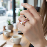 Close-up of a hand wearing a pink and gold ring with a blurred cafe background