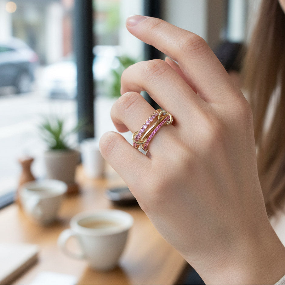 Close-up of a hand wearing a pink and gold ring with a blurred cafe background