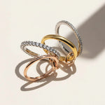 Set of four linked rings in gold, silver, and rose gold tones with cubic zirconia accents on beige background.