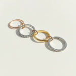 Four linked rings in silver, gold, and rose gold with cubic zirconia detailing, arranged in a row on light background.