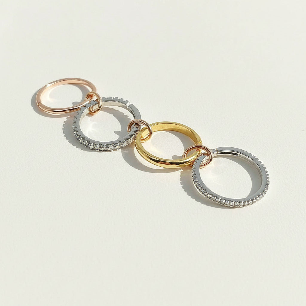 Four linked rings in silver, gold, and rose gold with cubic zirconia detailing, arranged in a row on light background.