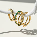 Four gold rings with green gemstones on a white surface