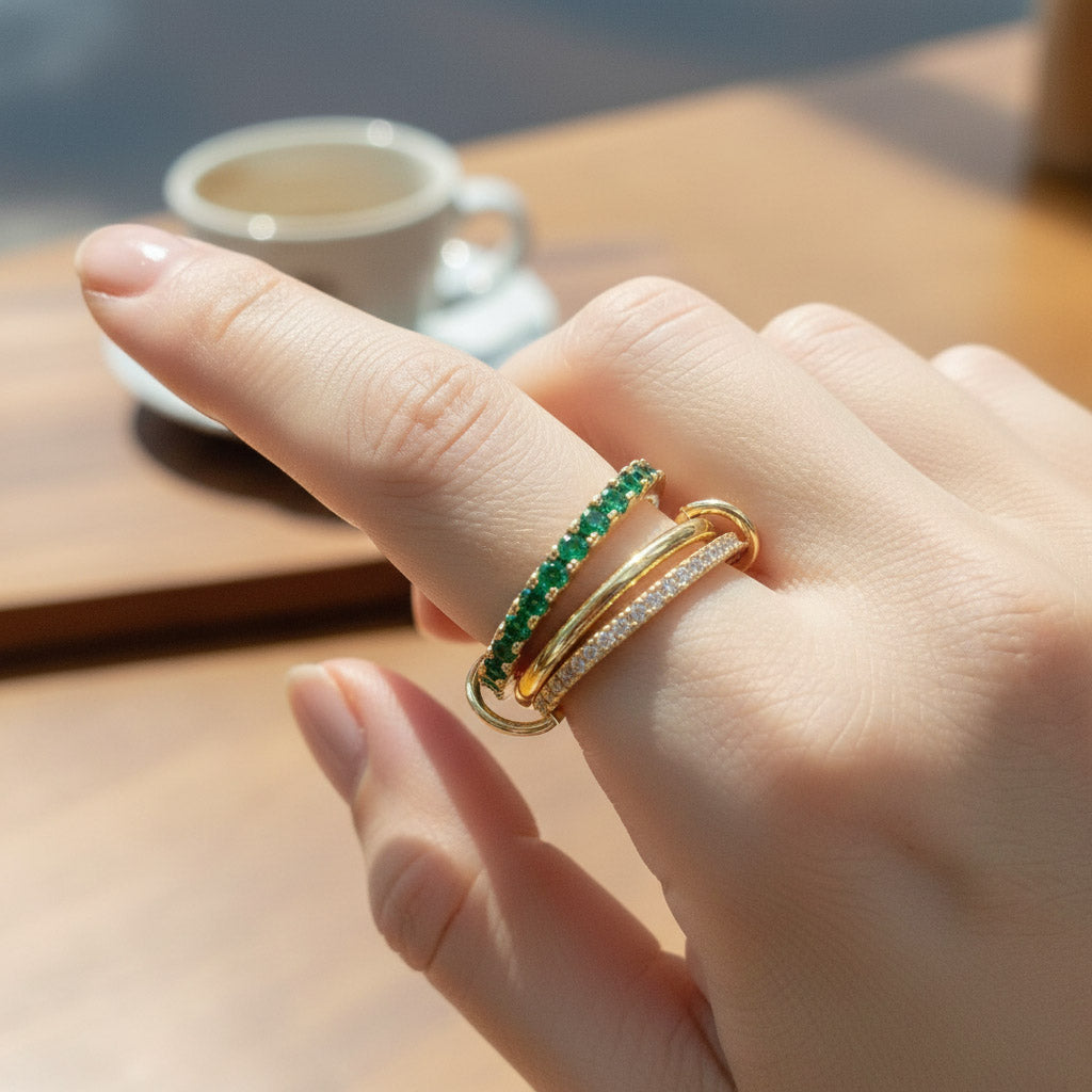 Hand wearing a gold ring with green gemstones on a blurred background