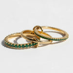 Three gold rings with green gemstones on a light gray background