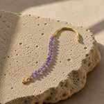 Amethyst gemstone hook bracelet with gold plated stainless steel details on textured stone surface