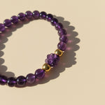 Amethyst gemstone bracelet with gold accents on a beige background