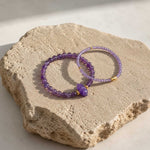 Amethyst beaded bracelet set on natural stone surface with gold accents
