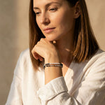 Woman wearing Zebra Jasper and freshwater pearl gemstone bracelets on her wrist against a neutral background