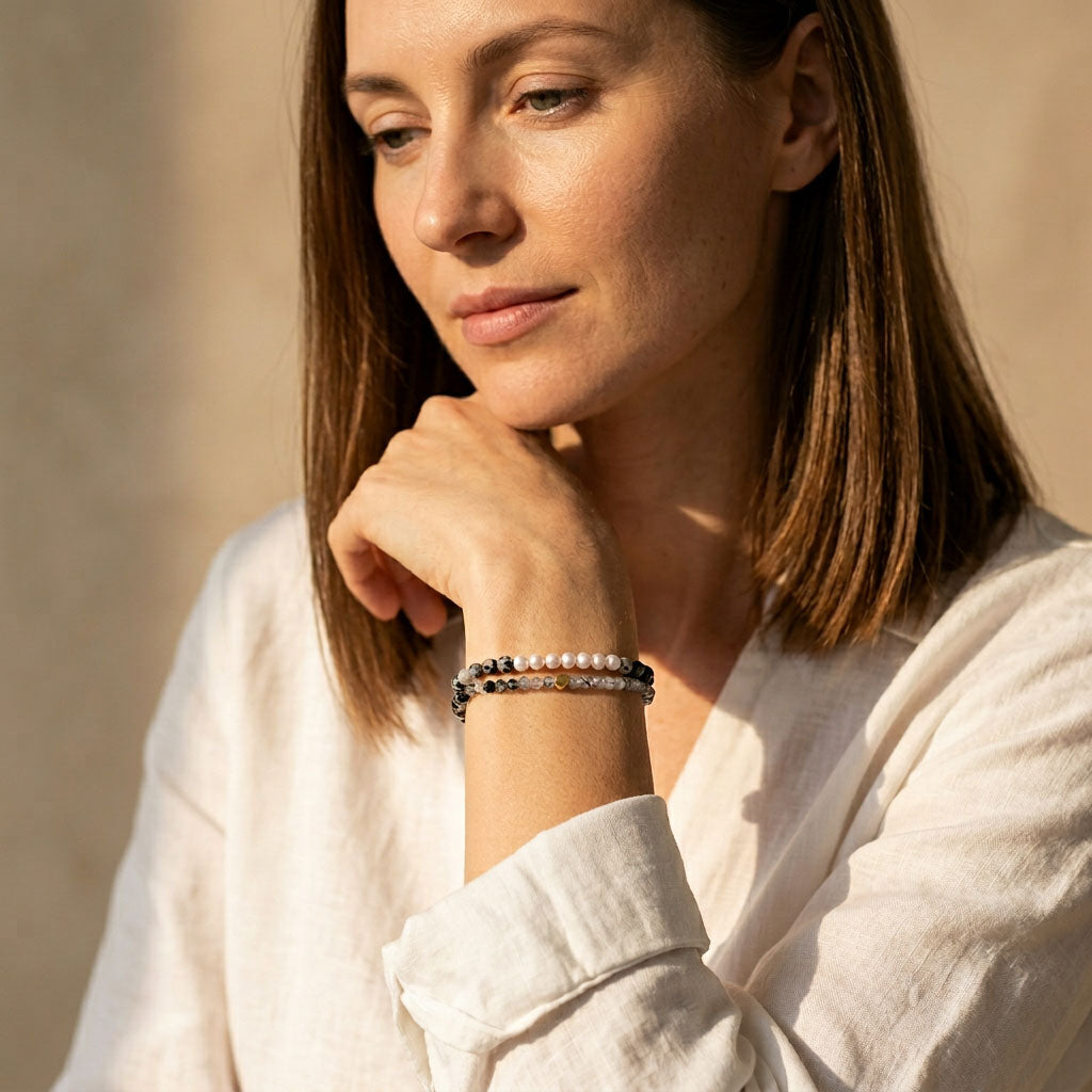 Woman wearing Zebra Jasper and freshwater pearl gemstone bracelets on her wrist against a neutral background