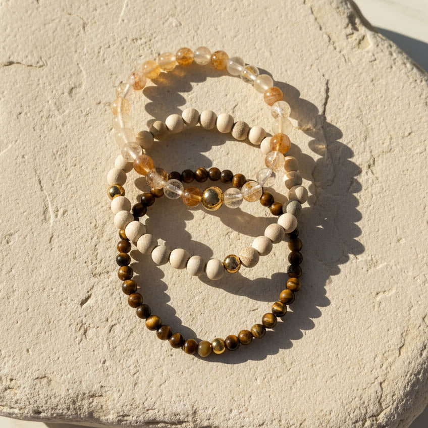 Tiger Eye Rutilated Quartz and camphor wood gemstone bracelets with gold bead on a textured stone surface