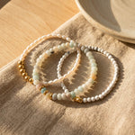 Three beaded bracelets on a textured fabric surface with a wooden background