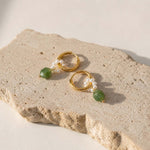Gold hoop earrings with pearl and green gemstone charms on sunlit stone