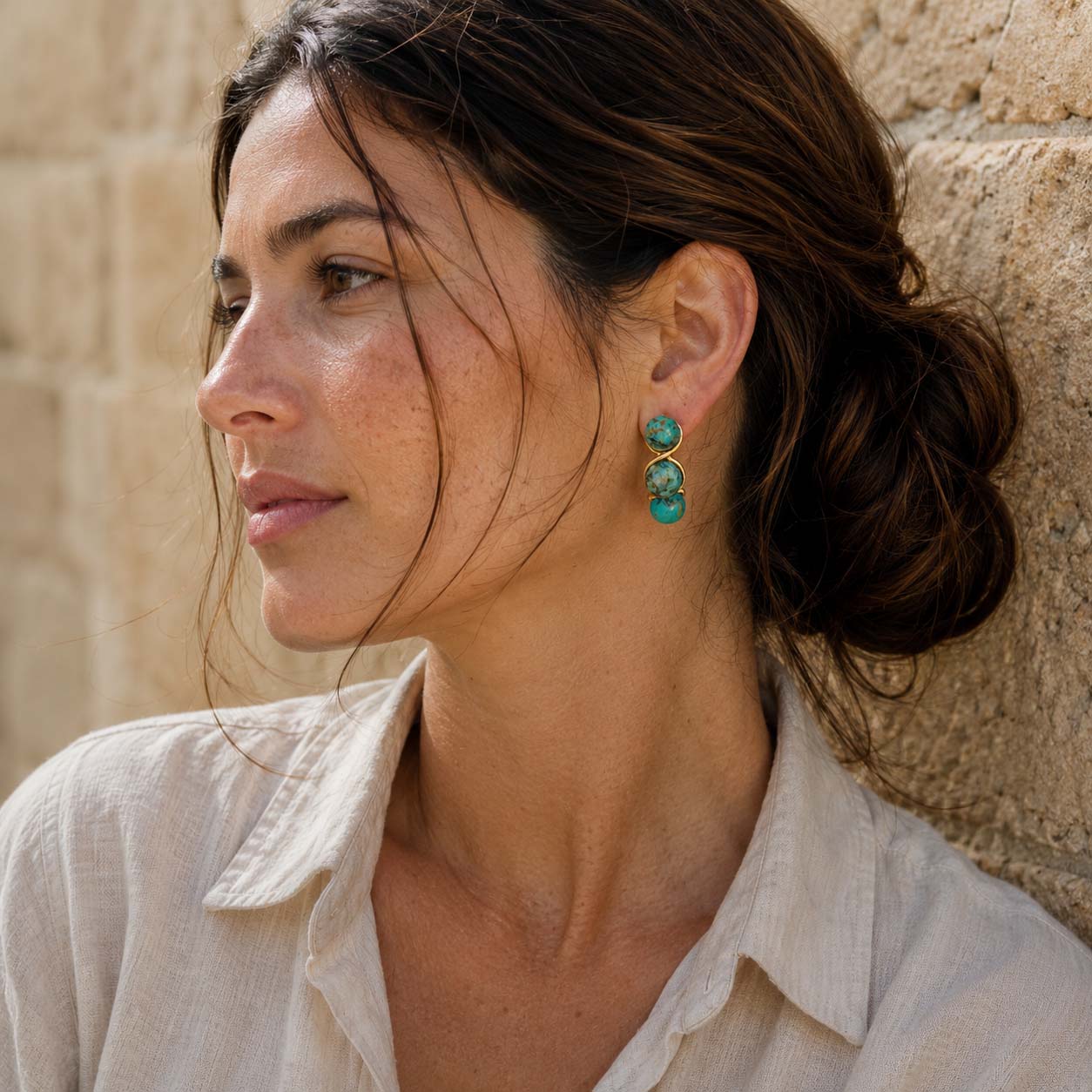 Woman wearing African Turquoise triple bead earrings against a stone wall