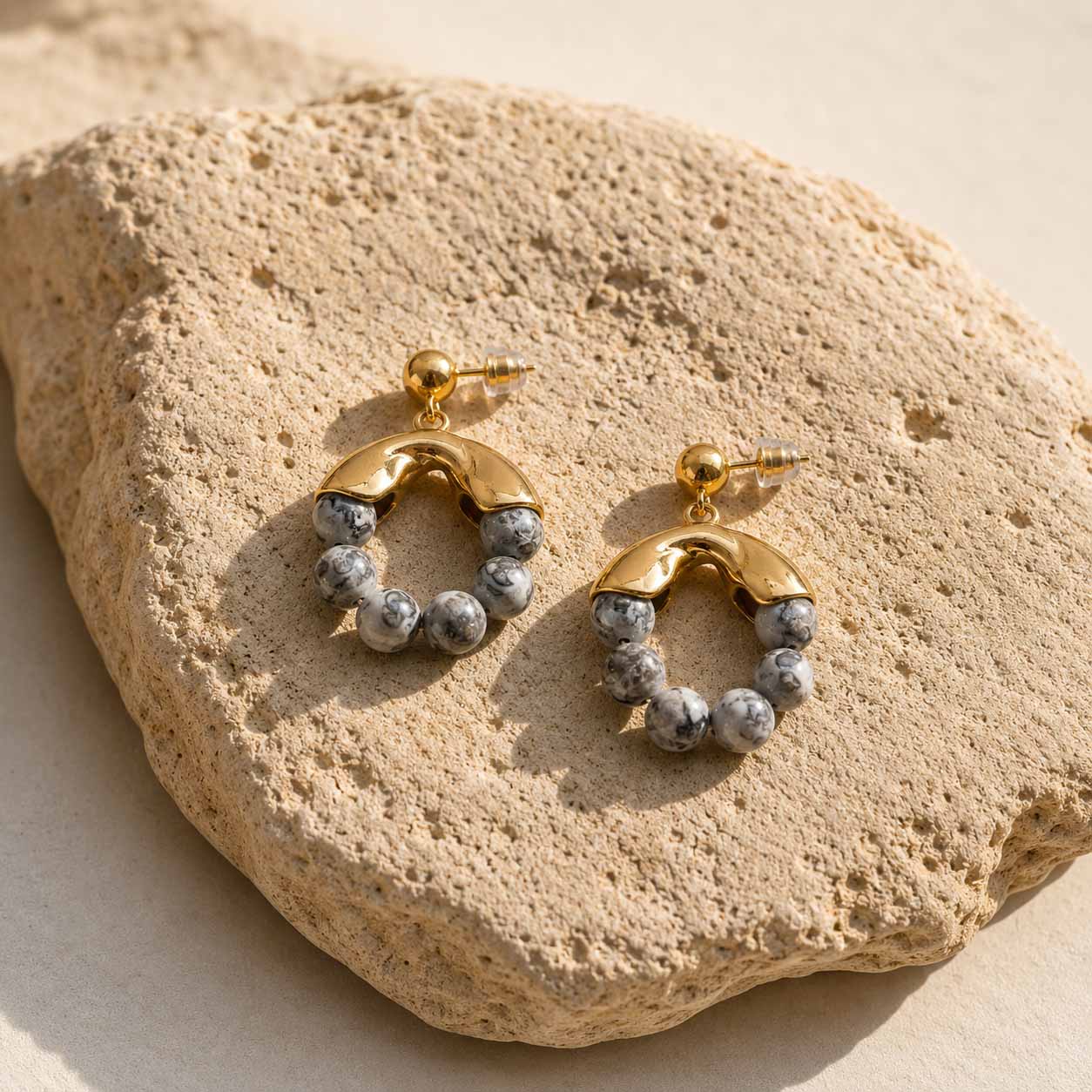 Gold beaded hoop earrings with grey Map Jasper stones on textured stone