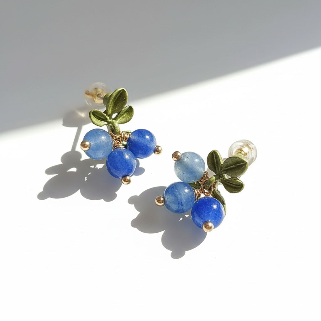 Pair of earrings with blueberry beads and green leaves on a white background