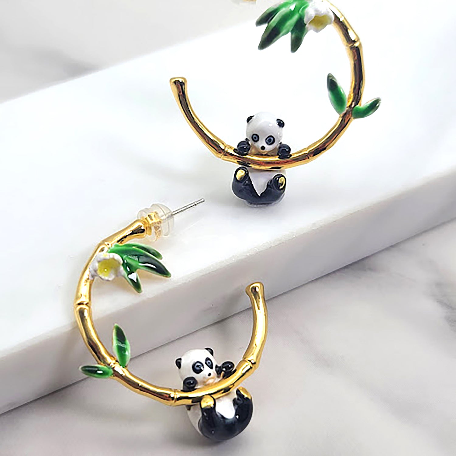 Gold bamboo hoop earrings with a playful panda design, featuring green leaf and yellow flower accents